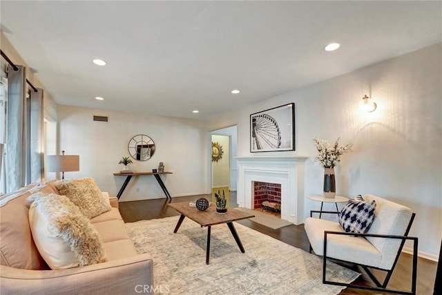 living room featuring a fireplace with flush hearth, visible vents, baseboards, recessed lighting, and wood finished floors