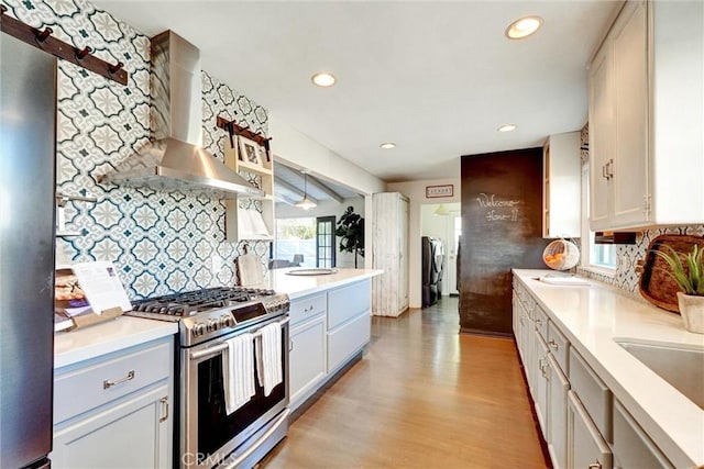 kitchen featuring light wood-style flooring, stainless steel appliances, wall chimney range hood, and decorative backsplash