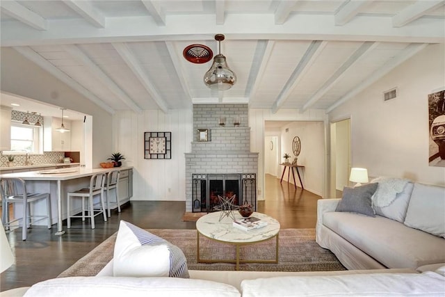 living room featuring dark wood finished floors, visible vents, vaulted ceiling with beams, and a fireplace