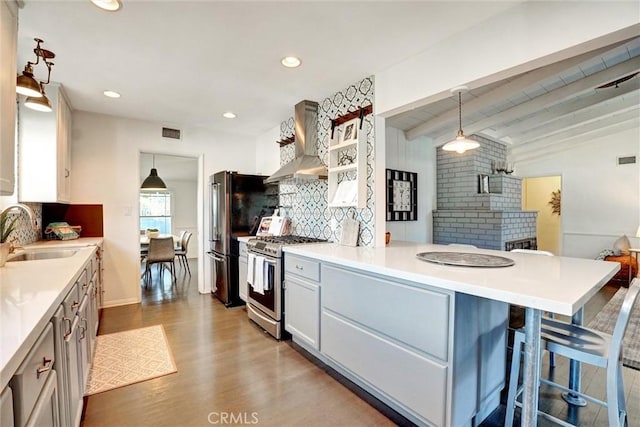 kitchen with a sink, appliances with stainless steel finishes, light wood-style floors, wall chimney exhaust hood, and a peninsula