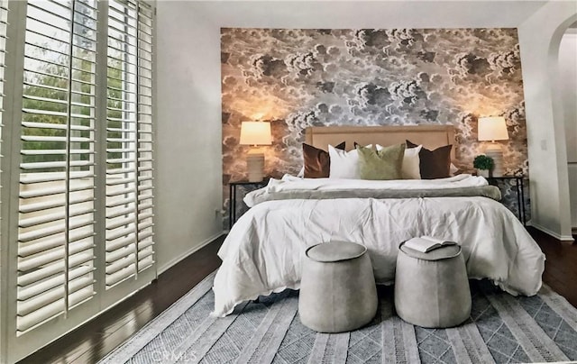 bedroom with baseboards, arched walkways, an accent wall, and wood finished floors