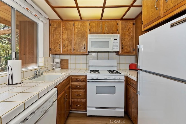 kitchen with brown cabinetry, tile countertops, a sink, and white appliances