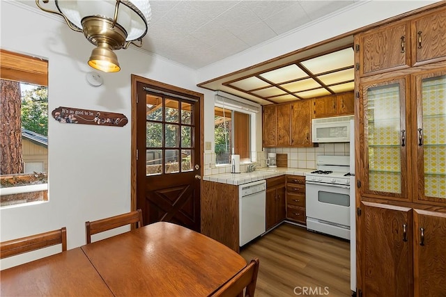 kitchen featuring white appliances, brown cabinetry, dark wood-type flooring, backsplash, and tile countertops