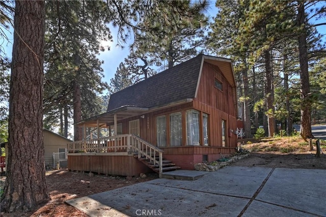 view of front of property with a wooden deck, a gambrel roof, and roof with shingles