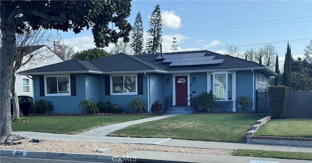 ranch-style house featuring roof mounted solar panels, stucco siding, fence, and a front lawn