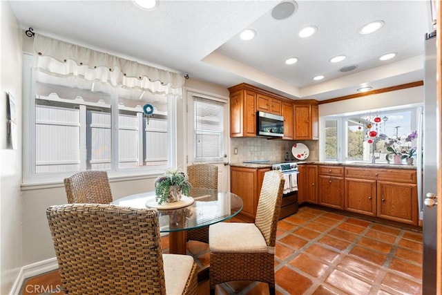 kitchen with appliances with stainless steel finishes, brown cabinets, a tray ceiling, recessed lighting, and decorative backsplash