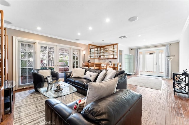 living area with french doors, visible vents, ornamental molding, and wood finished floors