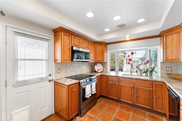kitchen with brown cabinetry, appliances with stainless steel finishes, a sink, and a tray ceiling