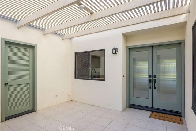 property entrance with a pergola, french doors, a patio area, and stucco siding