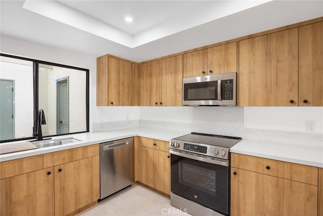 kitchen featuring a tray ceiling, a sink, light countertops, stainless steel appliances, and recessed lighting