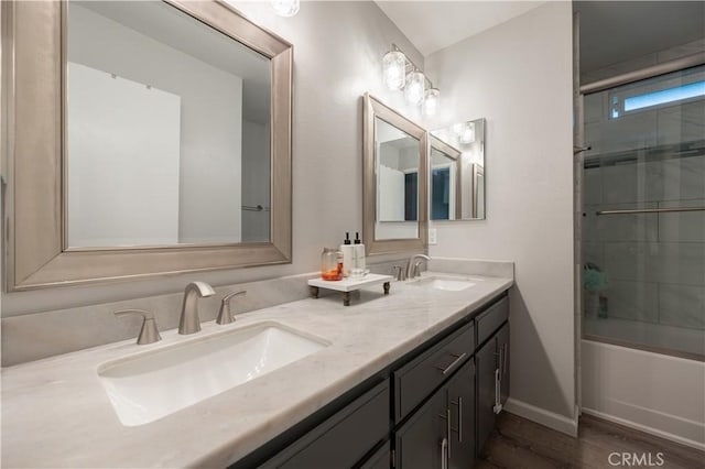 full bath with wood finished floors, double vanity, a sink, and combined bath / shower with glass door