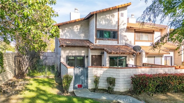 mediterranean / spanish-style house with a fenced front yard, a tiled roof, stucco siding, and a chimney