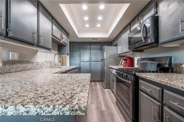 kitchen with light wood-type flooring, gas range oven, crown molding, a tray ceiling, and a sink