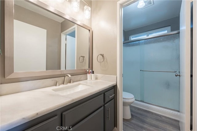 bathroom featuring vanity, toilet, a shower stall, visible vents, and wood finished floors