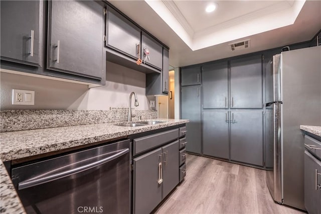 kitchen with crown molding, light wood-style floors, a tray ceiling, appliances with stainless steel finishes, and a sink