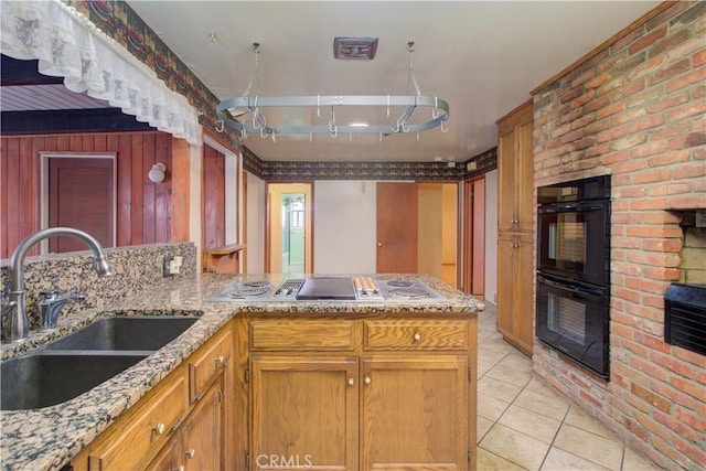 kitchen with light stone counters, dobule oven black, light tile patterned flooring, and a sink