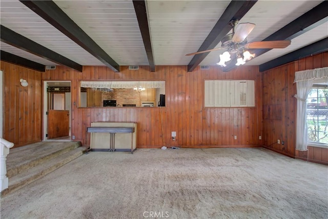 unfurnished living room featuring visible vents, ceiling fan, beam ceiling, carpet floors, and wood walls