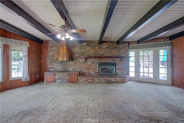 unfurnished living room with carpet, beam ceiling, wood walls, and a healthy amount of sunlight