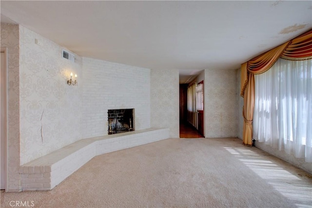 unfurnished living room featuring carpet, a brick fireplace, plenty of natural light, and visible vents