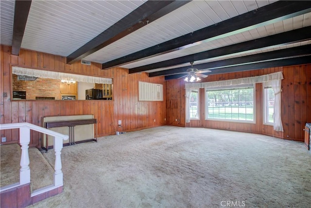 unfurnished living room featuring wood walls, visible vents, beam ceiling, carpet flooring, and ceiling fan