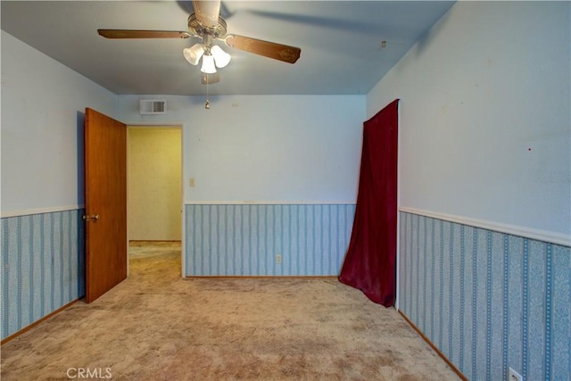 empty room featuring a wainscoted wall, visible vents, carpet, and ceiling fan
