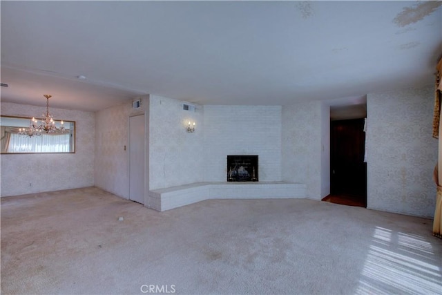 unfurnished living room featuring a chandelier, carpet flooring, a fireplace, and visible vents