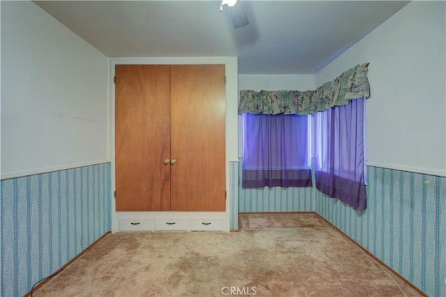 unfurnished bedroom featuring carpet flooring, ceiling fan, a wainscoted wall, and wallpapered walls