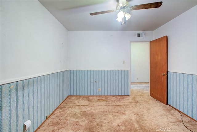 unfurnished room featuring visible vents, ceiling fan, carpet flooring, and wainscoting