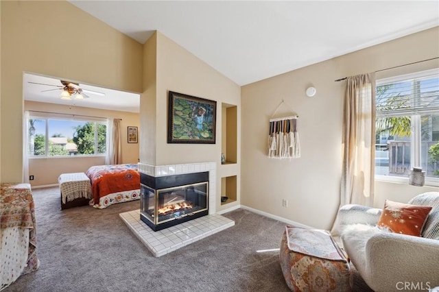 carpeted living area featuring a tiled fireplace, baseboards, vaulted ceiling, and ceiling fan