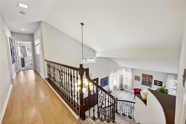 hallway with baseboards, an upstairs landing, wood finished floors, and vaulted ceiling