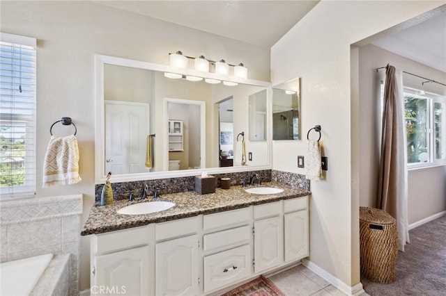 full bath featuring double vanity, tiled tub, a sink, and baseboards