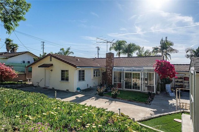 rear view of property featuring a chimney, stucco siding, a tiled roof, a patio area, and a lawn