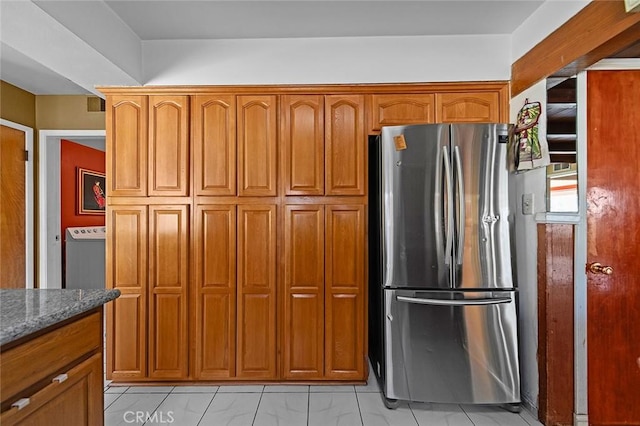 kitchen featuring dark stone countertops, marble finish floor, brown cabinets, and freestanding refrigerator