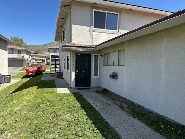 property entrance featuring a yard, a mountain view, stucco siding, and central AC unit