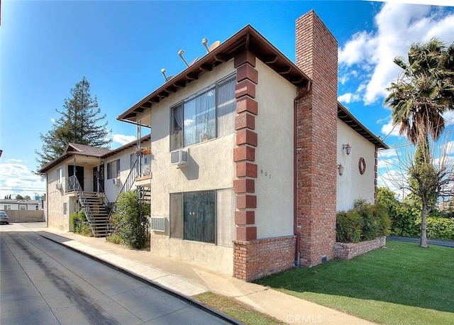 view of side of home featuring stairs, stucco siding, a chimney, and a lawn
