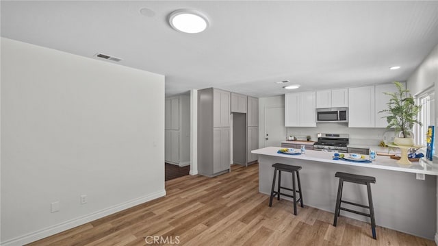 10069 Hershey Way, Riverside, CA 92503 - kitchen with appliances with stainless steel finishes, a peninsula, light countertops, a kitchen bar, and light wood-style flooring