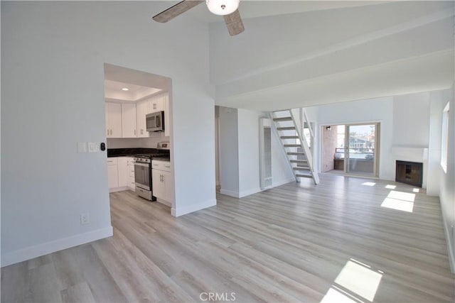 17114 Bluewater Ln Unit 141, Huntington Beach, CA 92649 - unfurnished living room with stairs, light wood-style floors, a ceiling fan, baseboards, and a towering ceiling