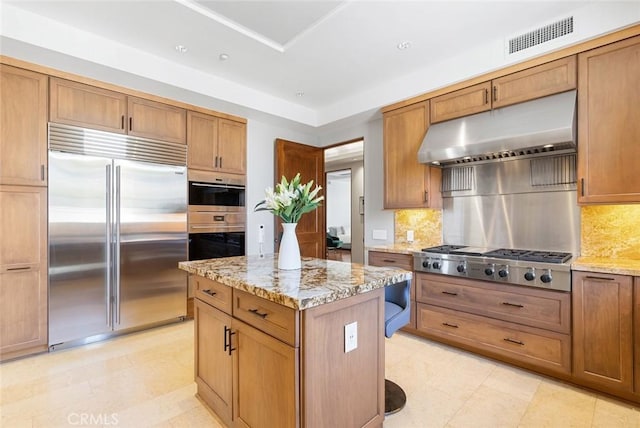kitchen with brown cabinetry, visible vents, under cabinet range hood, light stone counters, and stainless steel appliances