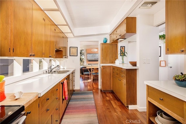 kitchen with dark wood-type flooring, brown cabinetry, visible vents, light countertops, and a sink