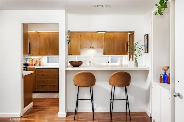 kitchen with a breakfast bar, light countertops, visible vents, brown cabinets, and wood finished floors