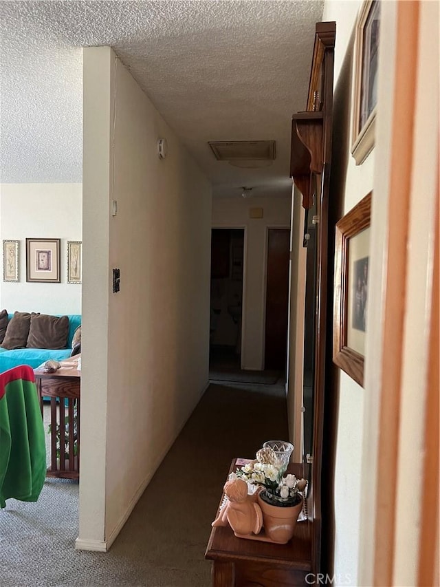 hall featuring dark carpet, a textured ceiling, and attic access