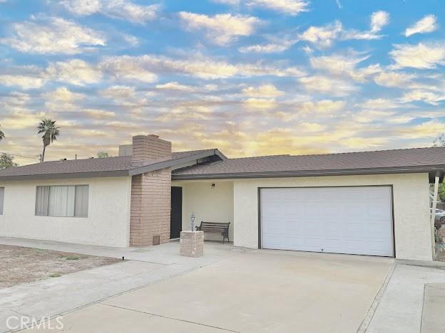 view of front of home with an attached garage, driveway, a chimney, and stucco siding