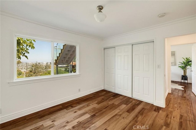 unfurnished bedroom with wood finished floors, crown molding, baseboards, and multiple windows