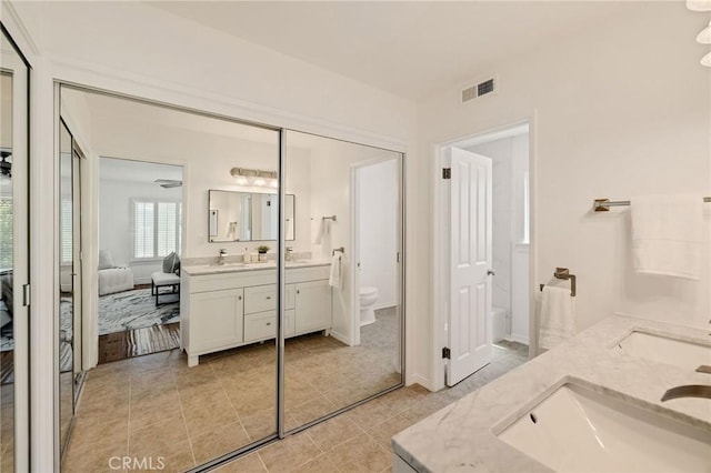 ensuite bathroom featuring toilet, a sink, double vanity, ensuite bath, and visible vents