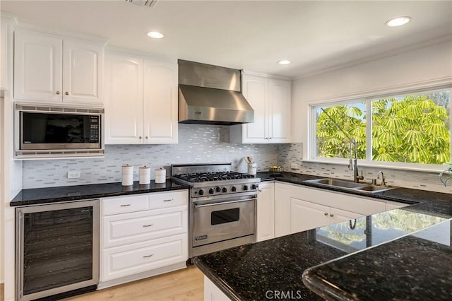 kitchen featuring beverage cooler, a healthy amount of sunlight, a sink, wall chimney exhaust hood, and appliances with stainless steel finishes