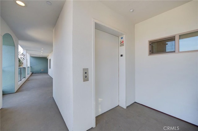 corridor featuring finished concrete floors, elevator, and recessed lighting