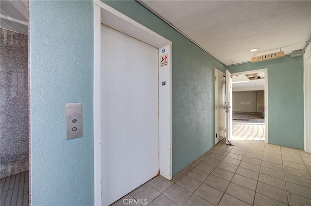 hallway with elevator, tile patterned floors, and a textured wall