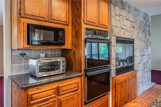 kitchen featuring brown cabinetry, tasteful backsplash, black appliances, dark stone countertops, and a toaster