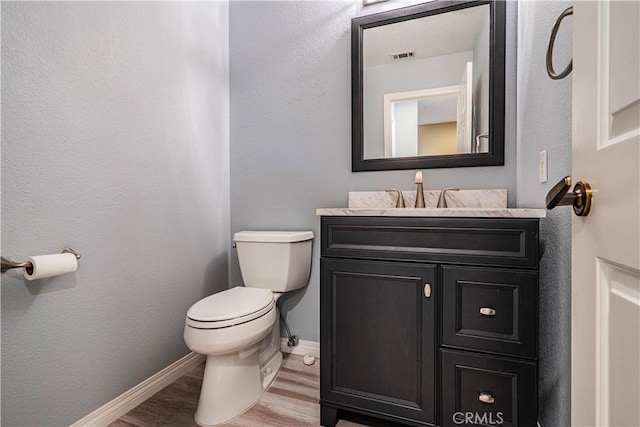 half bathroom featuring vanity, visible vents, toilet, wood finished floors, and baseboards