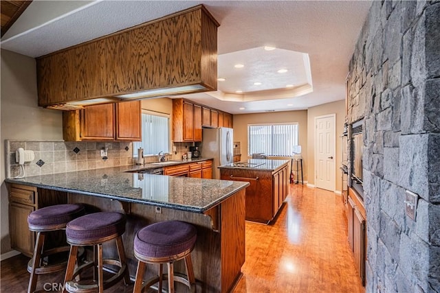 kitchen featuring a sink, freestanding refrigerator, brown cabinets, a tray ceiling, and a kitchen island